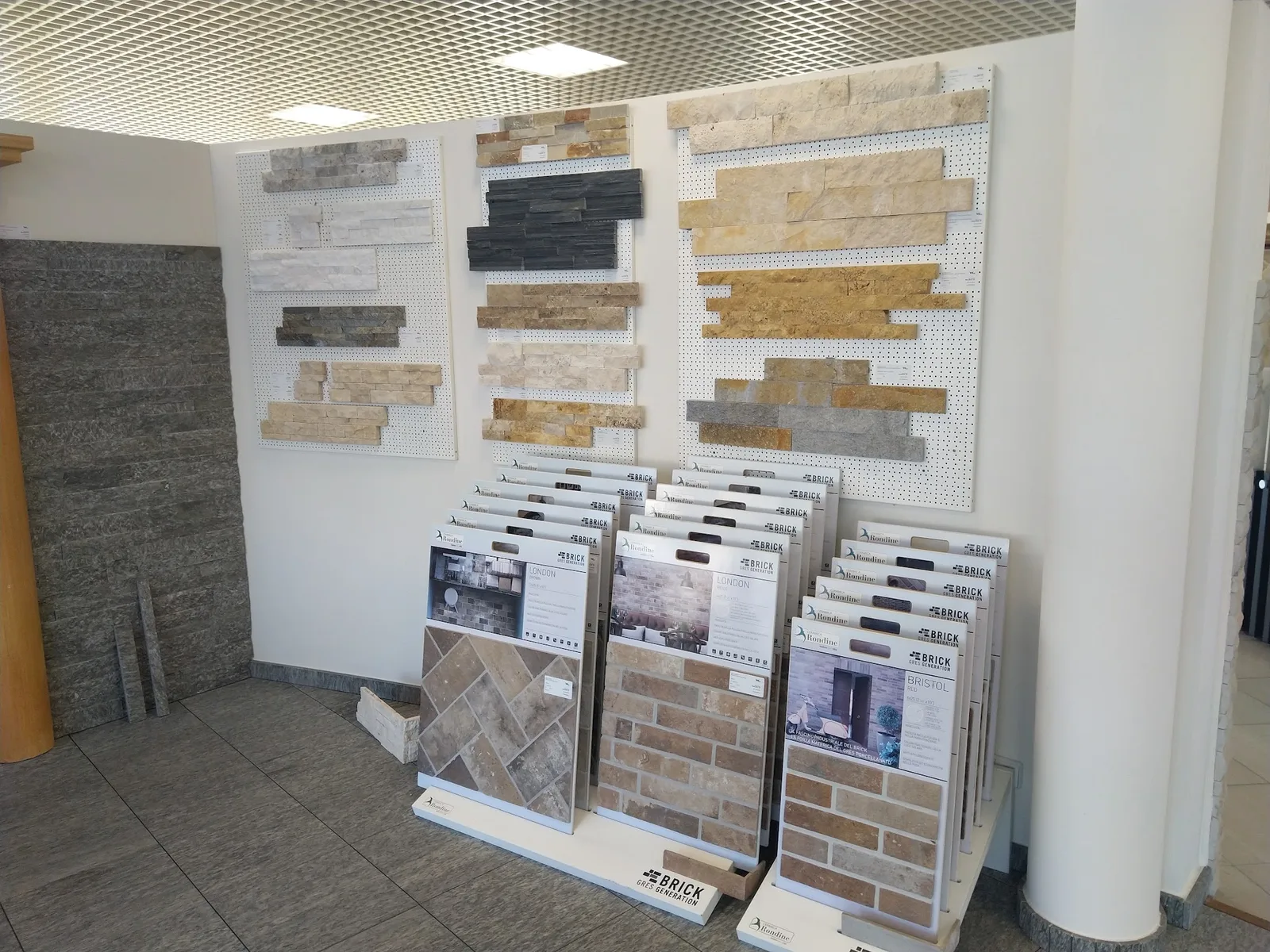 Natursteinmuster an einer Musterwand im Schauraum, davor Aufsteller mit Fliesenmustern